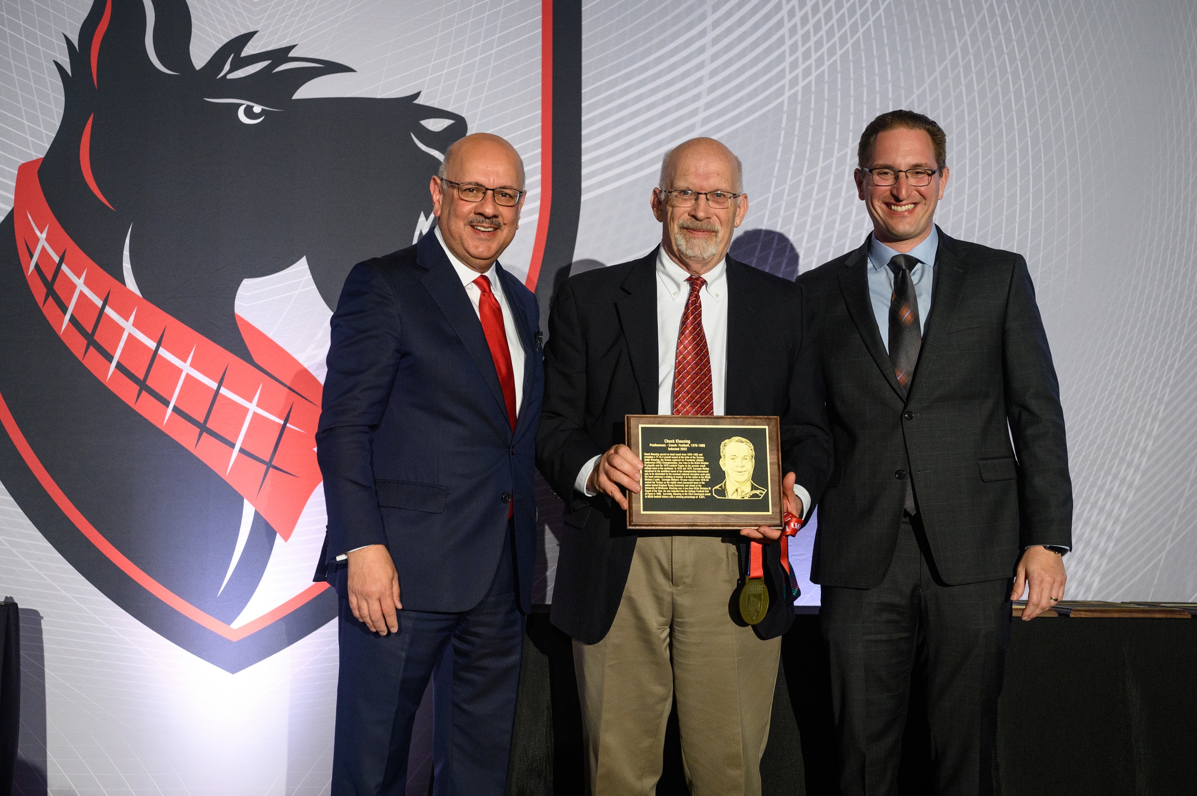 three men standing together with the one in the middle holding a plaque