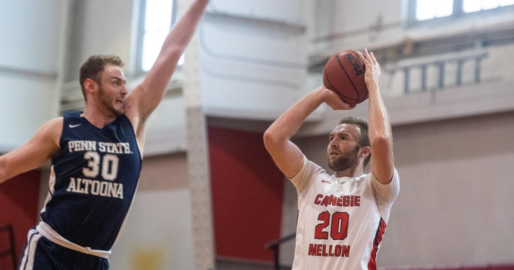 Basketball player in white taking a jump shot with a defender in blue lunging toward him