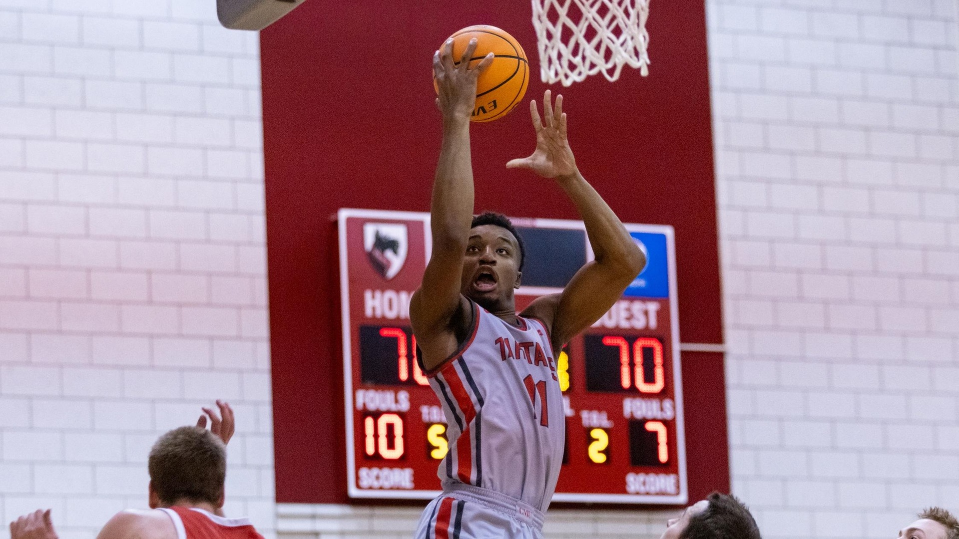 men's basketball player wearing a light gray uniform flies through air for a layup with three defenders nearby