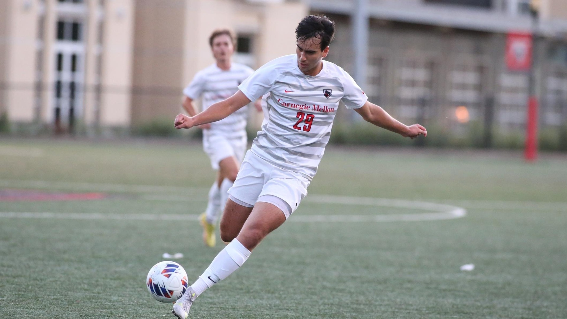 men's soccer player wearing a white uniform looks down while kicking the ball