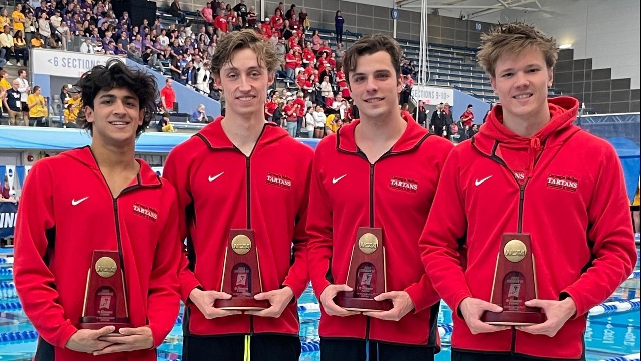four men wearing red full-zip jackets and black pants standing together and hold a trophy each