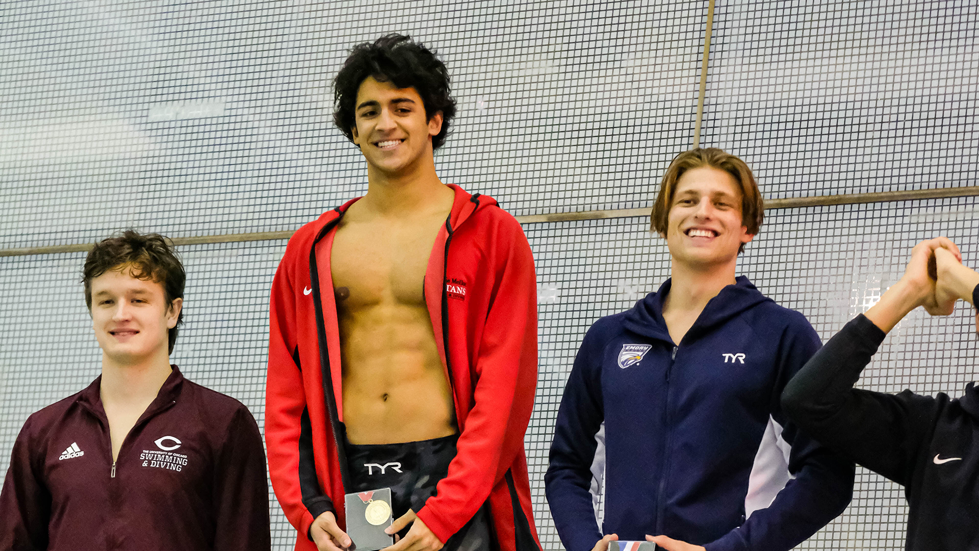 three men standing on a medal stand with person in the middle wearing a red jacket and holding a gold medal