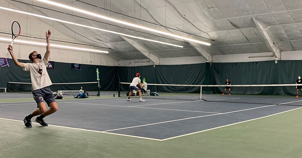Men's tennis player serving with a doubles partner at the net
