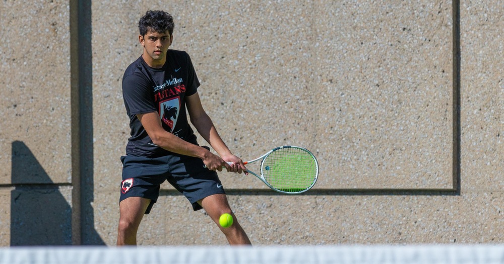 Men's tennis player wearing black shirt with gray shorts and about to hit a backhand shot