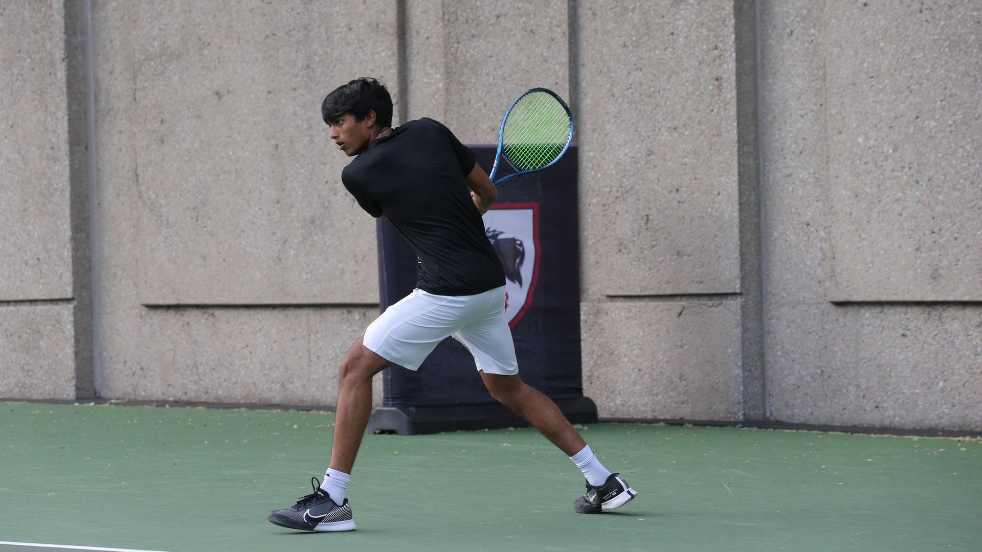 men's tennis player wearing a black shirt and white shorts preparing to swing the racquet