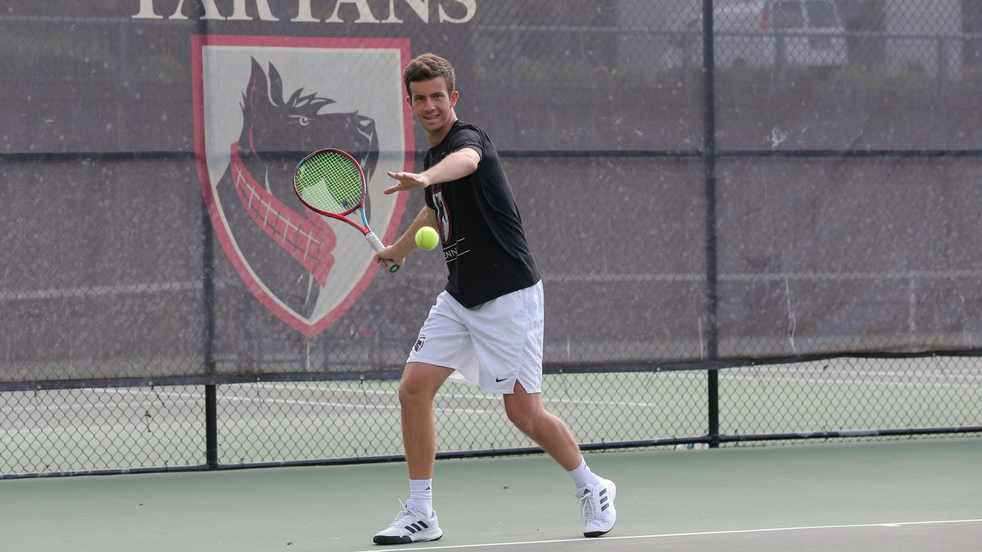 men's tennis player wearing black shirt and white shorts swings racquet with right hand at the ball