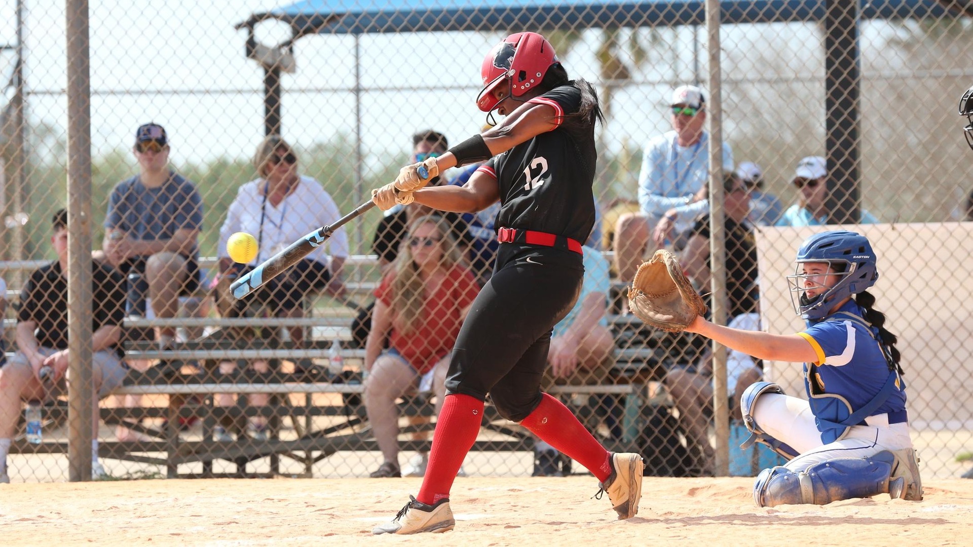 women's softball player wearing all black uniform makes contact with a pitch