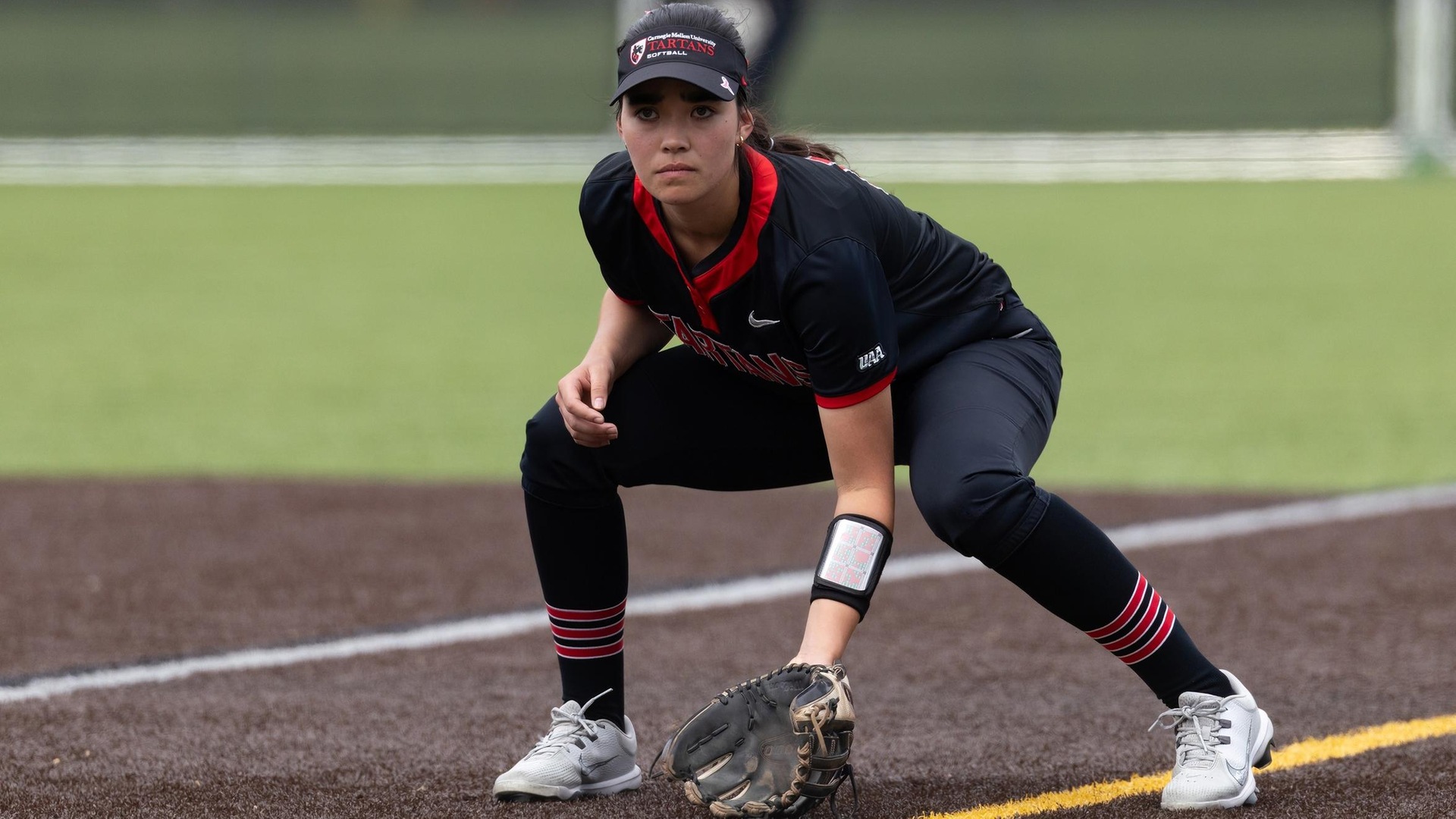 softball player wearing an all black uniform stands with glove on the ground preparing for a play
