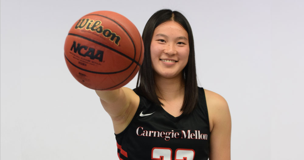 women's basketball player wearing black jersey and holding ball extended out in front of her