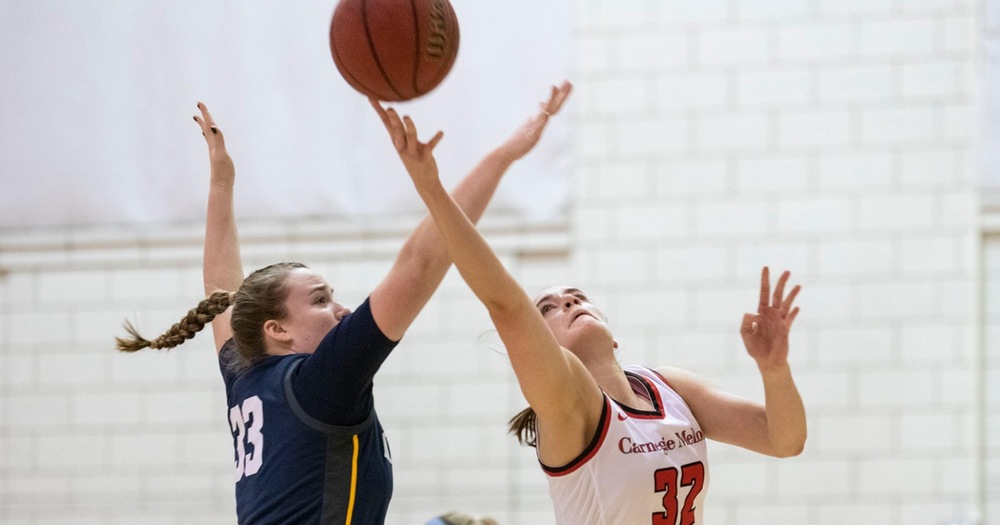 women's basketball player wearing white uniform taking a shot against a player in blue