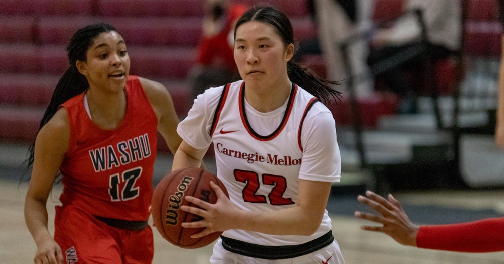 women's basketball player wearing white uniform driving between two defenders