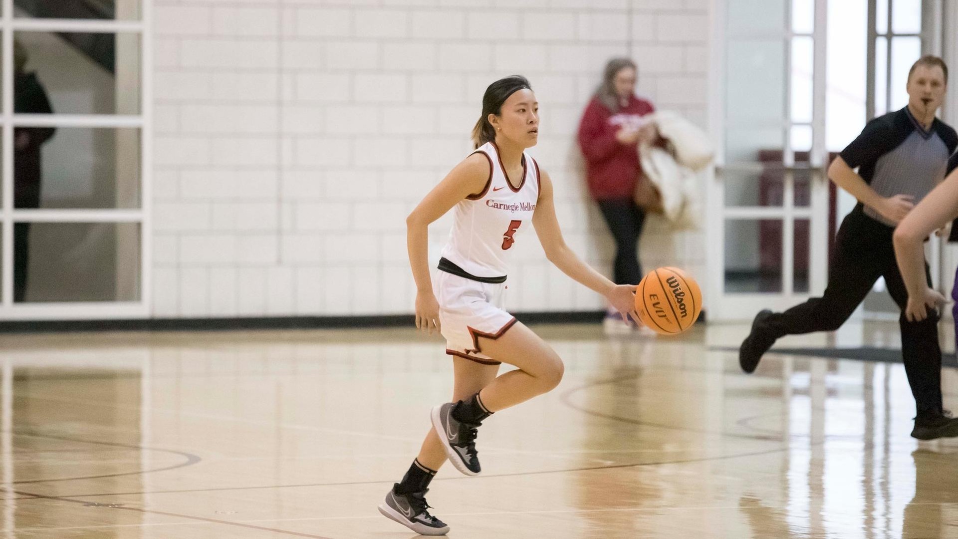 women's basketball player wearing a white uniform dribbling down the court