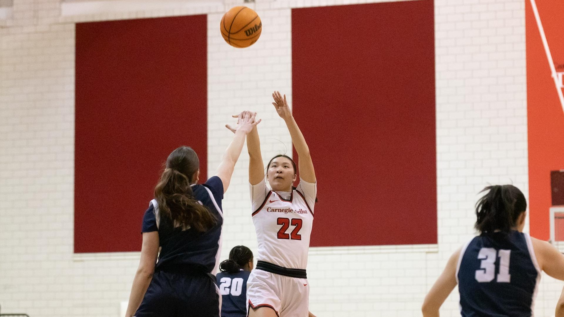 women's basketball player wearing a white uniform takes a shot over a player wearing a dark blue uniform