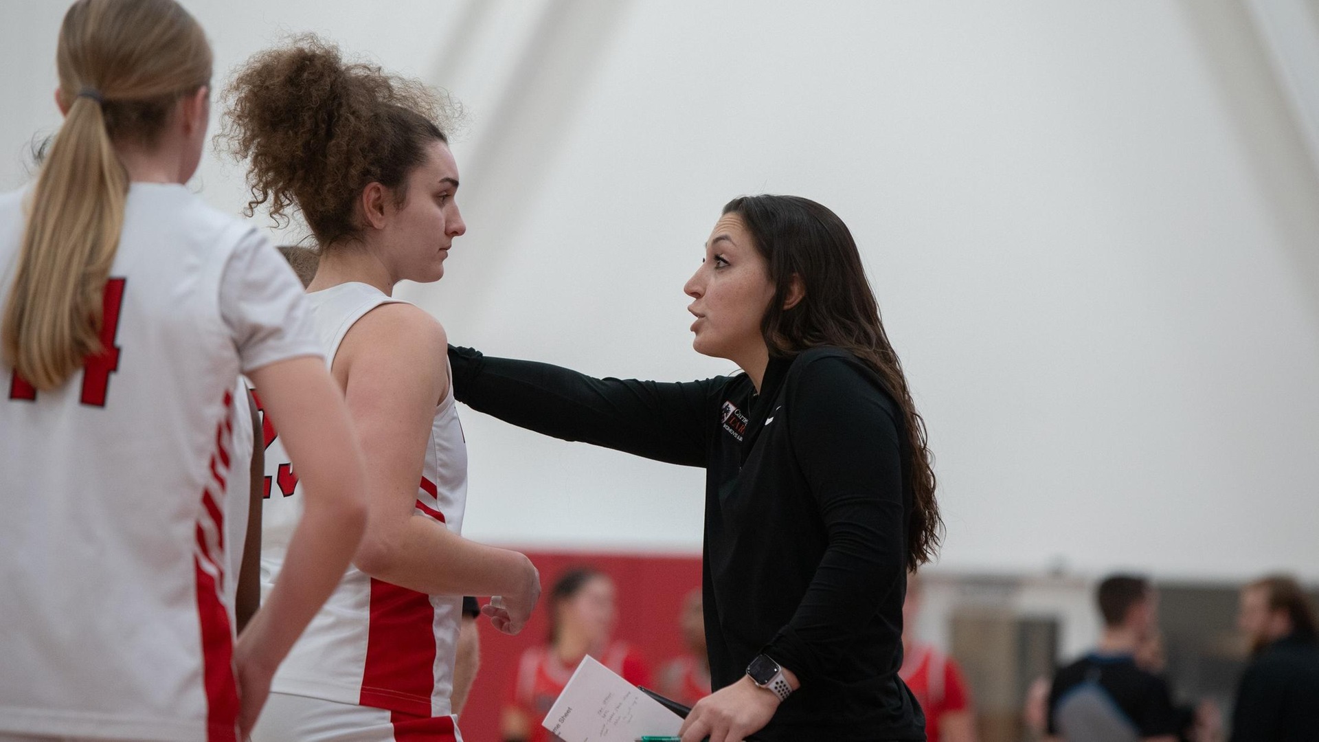 Two women's basketball players standing near the coach giving instruction