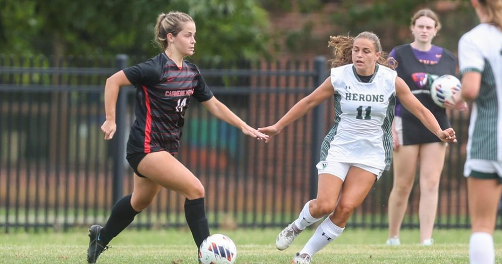women's soccer players, one wearing black uniform, one wearing a white uniform converge on the ball