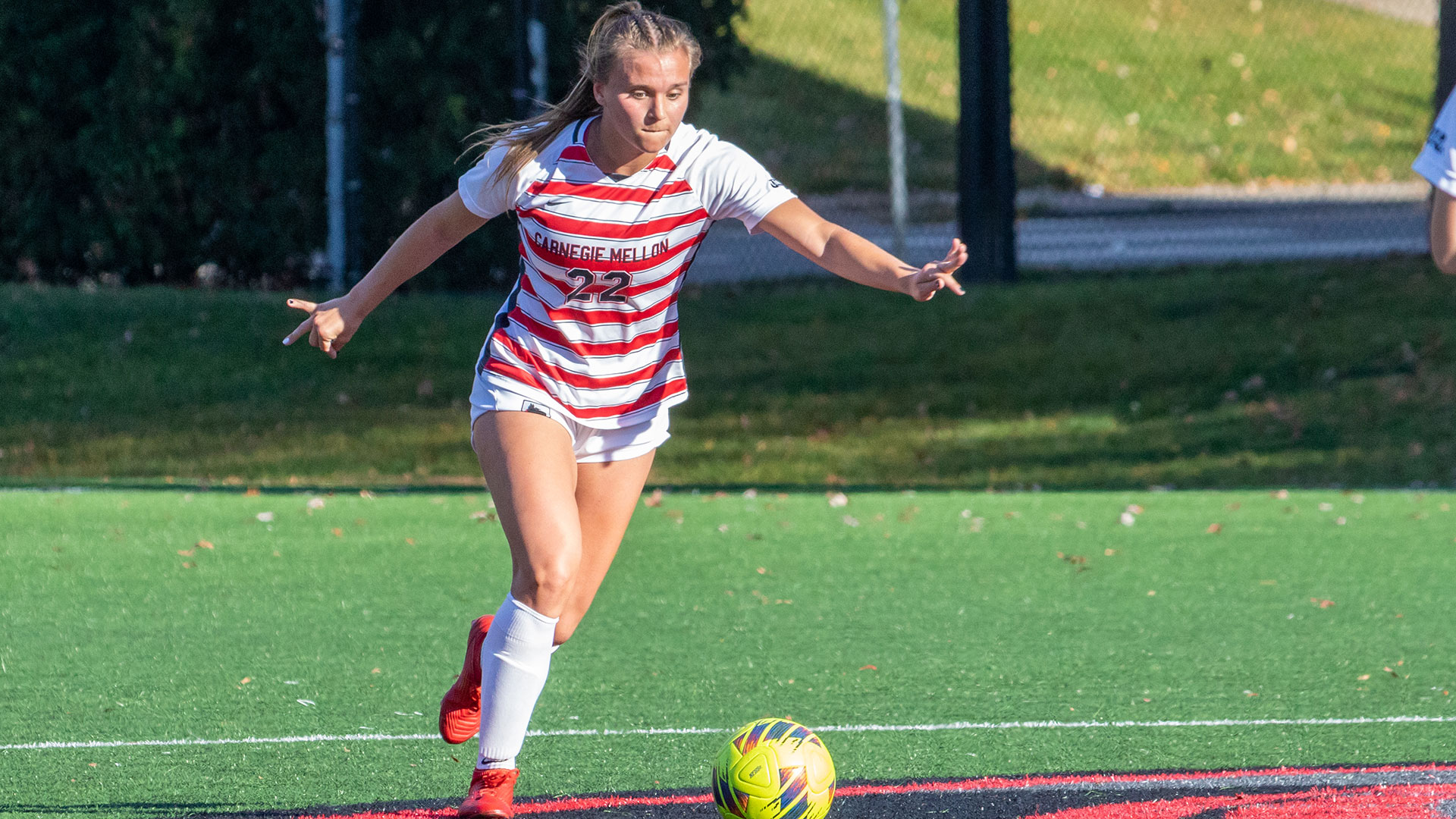 women's soccer player wearing a white and red striped jersey with white shorts prepares to kick a ball