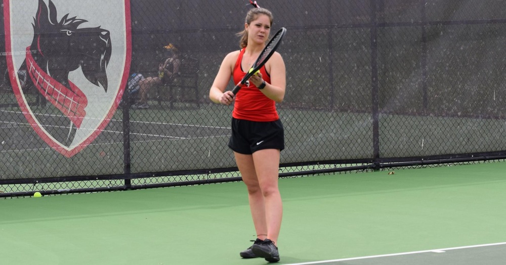 Women’s tennis player wearing red tank top and black skirt about to serve